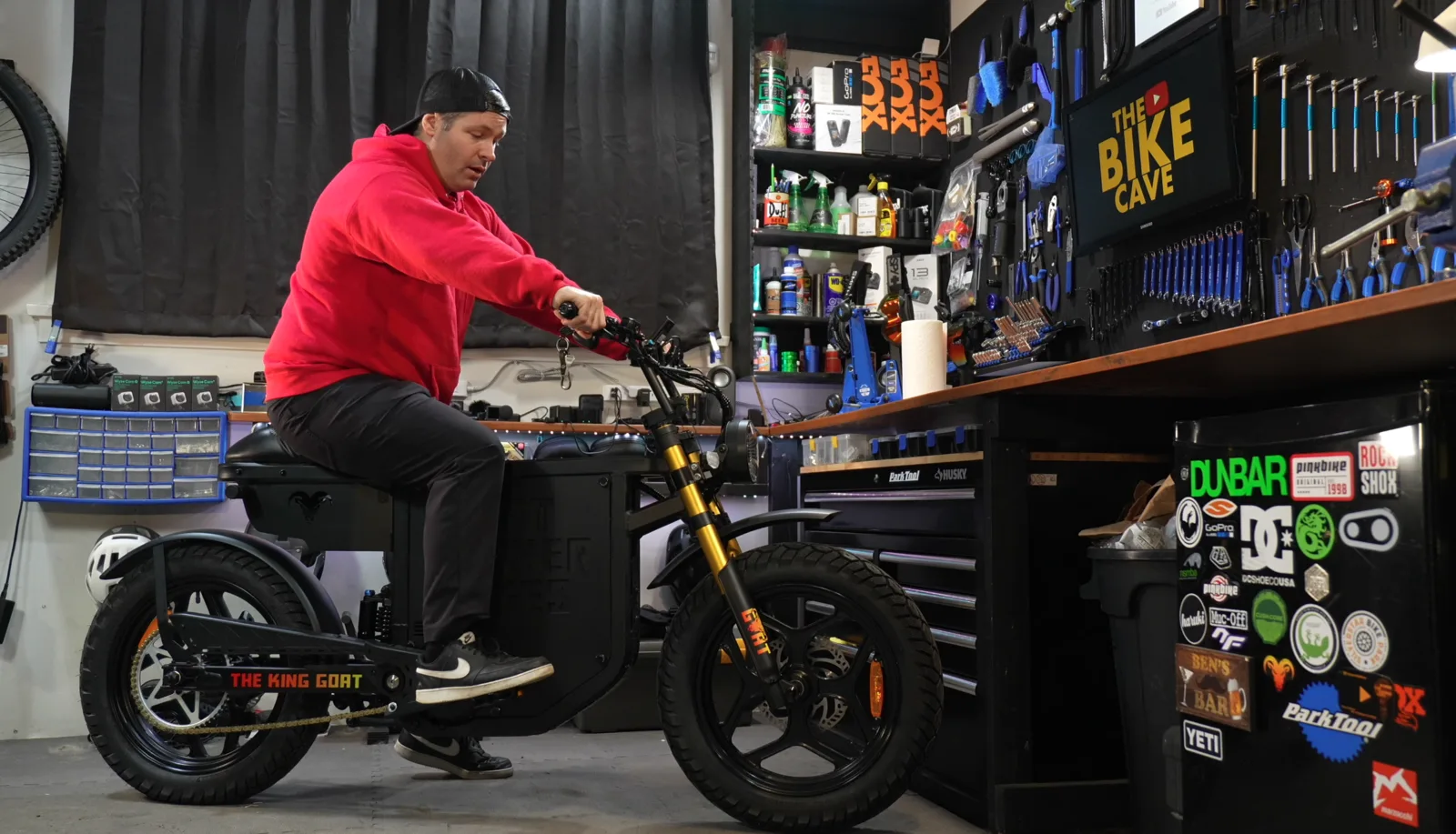Ben on the King Goat V3 in The Bike Cave garage, showing real-world scale